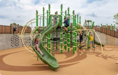 Green playground equipment with curved slide in front.