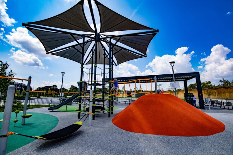 Large heptagon shade structure over orange and green mounds.