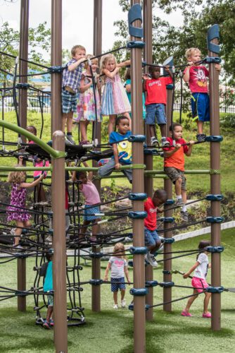 Large group of kids playing on climbing area of playground.
