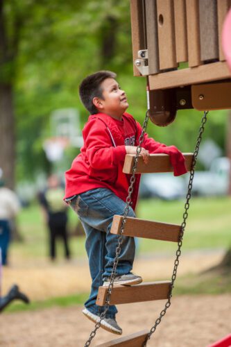 Kid in red sweater climbing rope ladder.