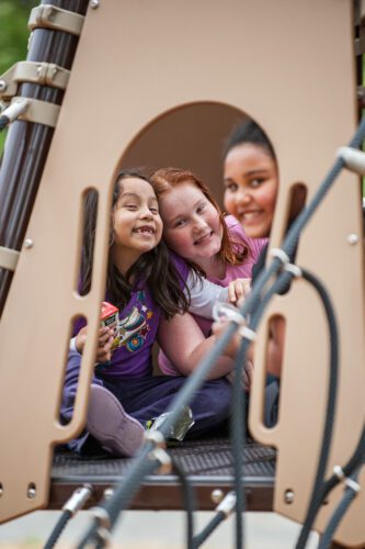 3 girls smiling from freestanding playground equipment.