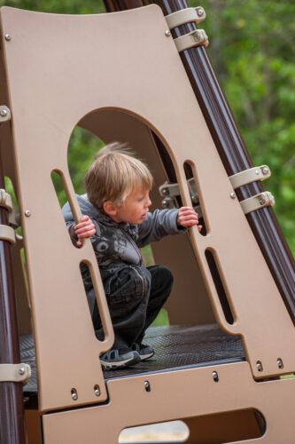 Kid peeking out from freestanding playground equipment.
