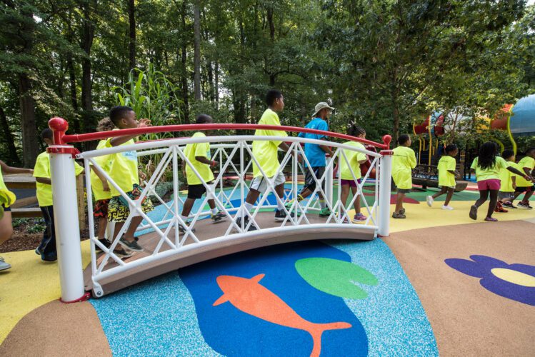 Kids crossing over bridge with surfacing below that looks like pond with fish.