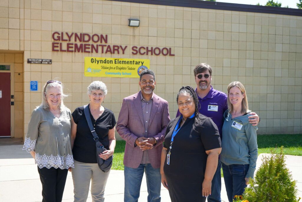 Group in front of elementary school smiling and shaking hands.