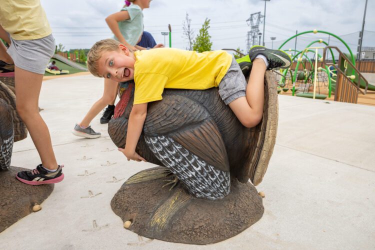 Smiling boy laying across turkey statue.