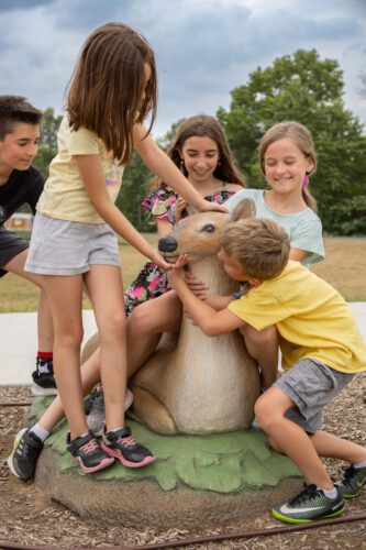 Group of young kids hugging deer statue.