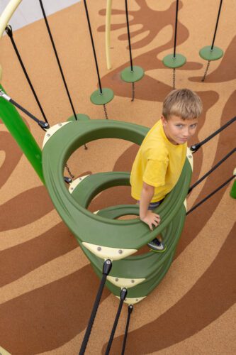 Boy in yellow shirt playing in tall playground equipment.