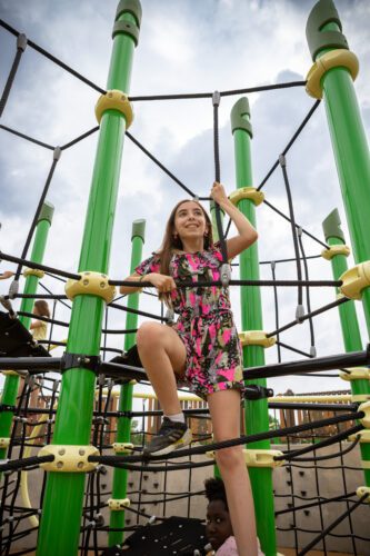 Girl in colorful outfit playing on net playground equipment,