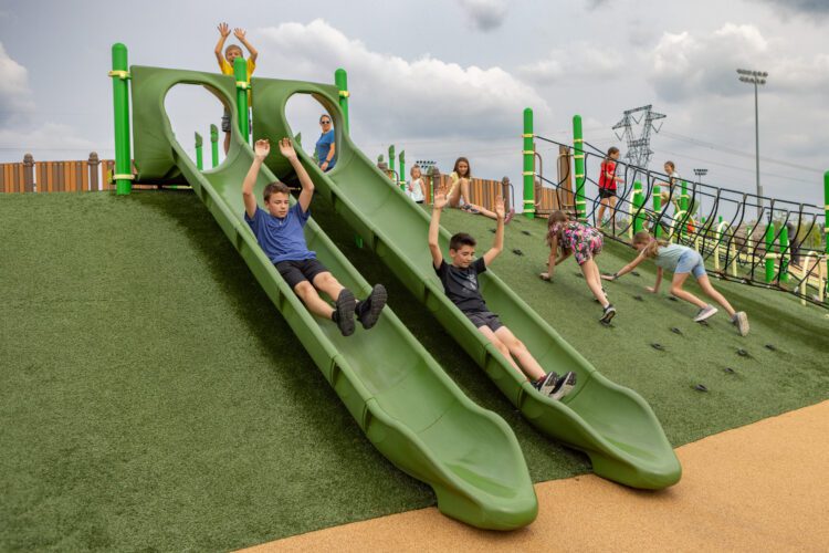 2 boys going down green slides, side by side.