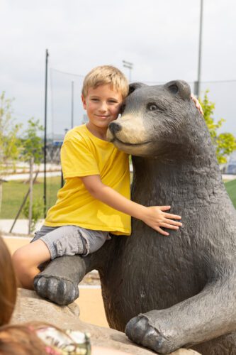 Boy in yellow shirt sitting with bear statue.