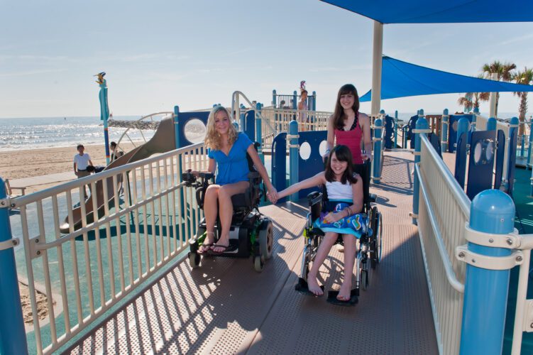 3 girls, 2 in wheelchairs, going down ramp from playground