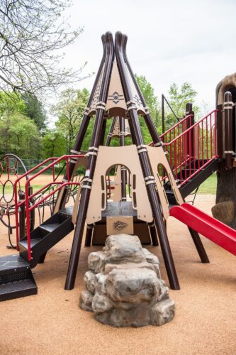 Custom teepee play structure with a connecting bridge, nature play elements, and slide at the Indian Creek Playground in Berwyn Heights, MD, installed by Sparks at Play using LSI equipment.