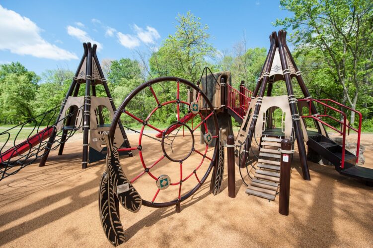 Overview of the Indian Creek Playground in Berwyn Heights, MD, featuring custom teepee play structures, nature play elements, and colorful pour-in-place surfacing, installed by Sparks at Play using LSI equipment.