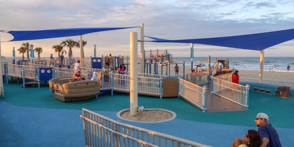 Overview of JT's Grommet Island Beach Park Playground for EveryBODY in Virginia Beach, VA, featuring inclusive play equipment, SkyWays® shading, and colorful Poured-in-Place surfacing, installed by Sparks at Play using LSI equipment.
