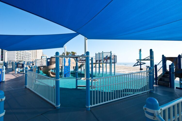 Overview of the play structure and LSI SkyWays® shade structure at JT's Grommet Island Beach Park Playground for EveryBODY in Virginia Beach, VA, installed by Sparks at Play.