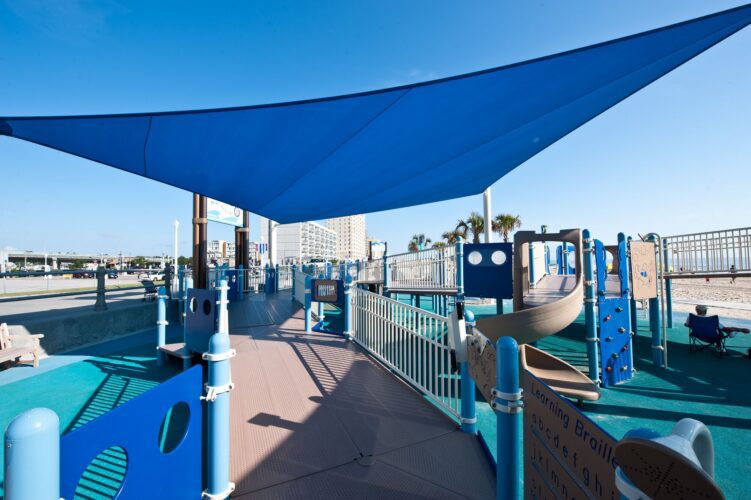 Overview of the play structure and LSI SkyWays® shade structure at JT's Grommet Island Beach Park Playground for EveryBODY in Virginia Beach, VA, installed by Sparks at Play.