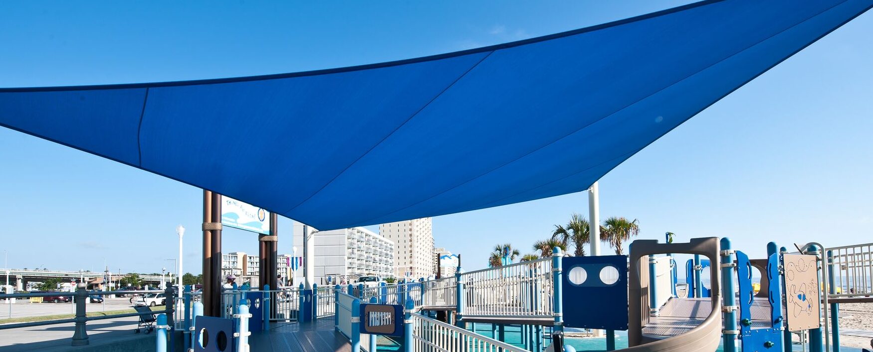 Overview of the play structure and LSI SkyWays® shade structure at JT's Grommet Island Beach Park Playground for EveryBODY in Virginia Beach, VA, installed by Sparks at Play.