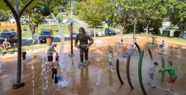 Overview of the City of Norton splash pad in Norton, Virginia, featuring the Wood Booger GFRC statue, Aquatix water play elements, pine tree showers, and ground sprays, installed by Sparks at Play.