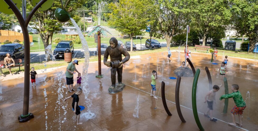 Overview of the City of Norton splash pad in Norton, Virginia, featuring the Wood Booger GFRC statue, Aquatix water play elements, pine tree showers, and ground sprays, installed by Sparks at Play.