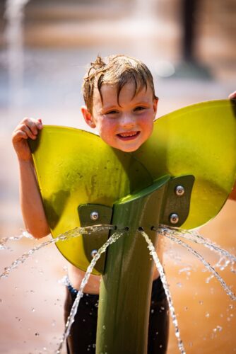 A boy exploring the Tot Wellspring with acrylic water feature at the City of Norton splash pad in Norton, Virginia, providing gentle sensory water play for toddlers, installed by Sparks at Play using Aquatix equipment.