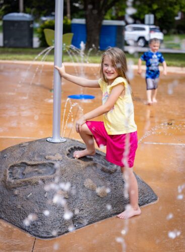 A little girl placing her foot inside a Wood Booger footprint at the City of Norton splash pad in Norton, Virginia, installed by Sparks at Play.