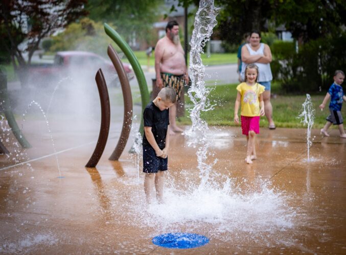 A boy getting soaked by ground spray water features at the City of Norton splash pad in Norton, Virginia, enjoying full sensory water play, installed by Sparks at Play using Aquatix equipment.