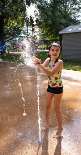 A girl playing with ground spray water features at the City of Norton splash pad in Norton, Virginia, enjoying sensory water play, installed by Sparks at Play using Aquatix equipment.
