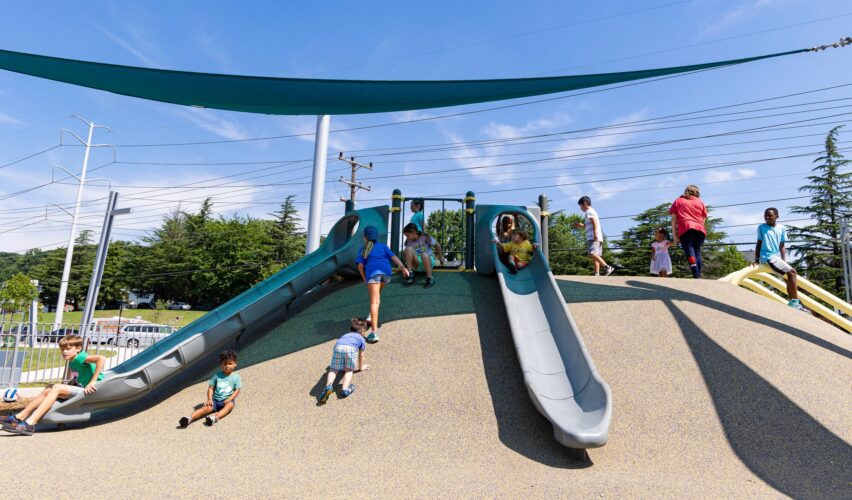 SlideWinder2® slide on an elevated hill with LSI SkyWays® shade overhead at the Jennie Dean Park playground in Arlington, VA, installed by Sparks at Play.