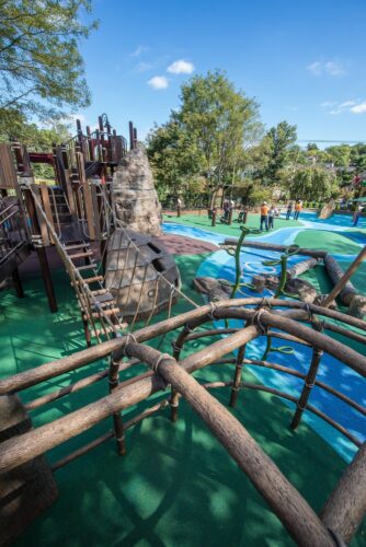 Overview of the Palisades Recreation Center playground in Washington, DC, featuring native-themed climbing structures, cargo-net bridges, and river-themed Poured-in-Place surfacing, installed by Sparks at Play using LSI equipment.