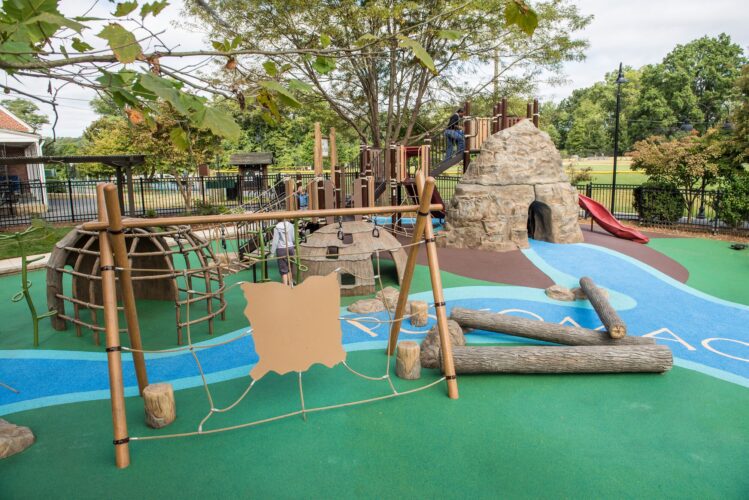 Overview of the Palisades Recreation Center playground in Washington, DC, featuring native-themed climbing structures, cargo-net bridges, and river-themed Poured-in-Place surfacing, installed by Sparks at Play using LSI equipment.
