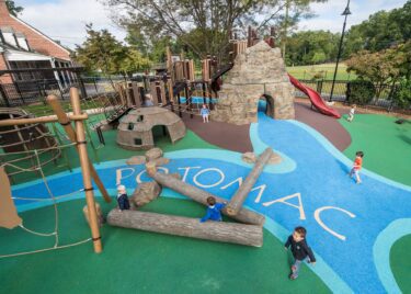 Overview of the Palisades Recreation Center playground in Washington, DC, featuring native-themed climbing structures, cargo-net bridges, and river-themed Poured-in-Place surfacing, installed by Sparks at Play using LSI equipment.