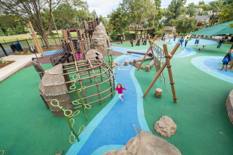 Overview of the Palisades Recreation Center playground in Washington, DC, featuring native-themed climbing structures, cargo-net bridges, and river-themed Poured-in-Place surfacing, installed by Sparks at Play using LSI equipment.