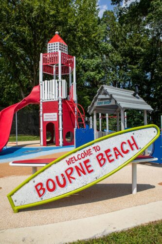 Custom surfboard sign at beach-themed playground J. Franklyn Bourne Park with lighthouse tower in background