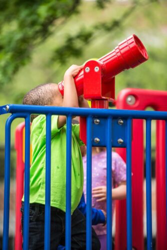 A young child looking through a periscope panel at the Prince George's County Childcare playground in Upper Marlboro, MD, installed by Sparks at Play using LSI equipment.